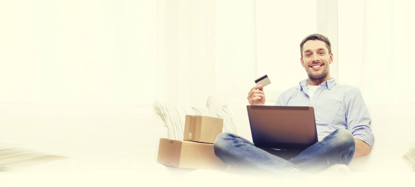 Rapaz sentado no chão com o seu portátil no colo e com um cartão na mão, ao lado dele estão caixas de cartão.